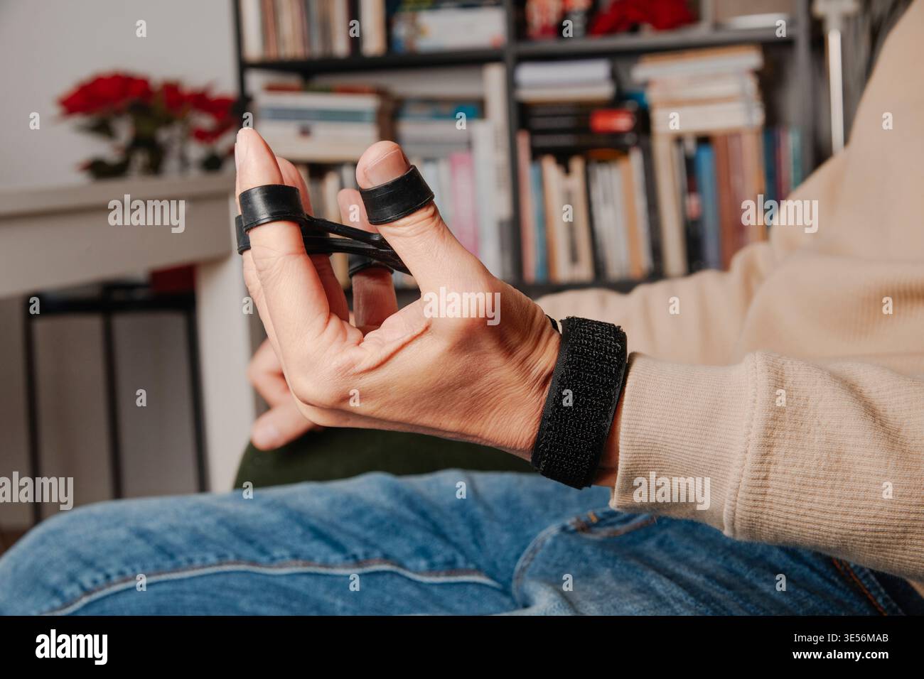 vue latérale d'un homme étirant un dispositif de bande de résistance des doigts assis à la maison, améliorant la force de préhension et la mobilité de la main avec un entraînement simple a Banque D'Images