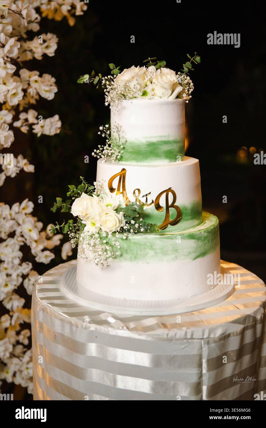 Élégant gâteau de mariage à trois niveaux orné de fleurs fraîches et de verdure, symbolisant l'amour et la célébration. Banque D'Images