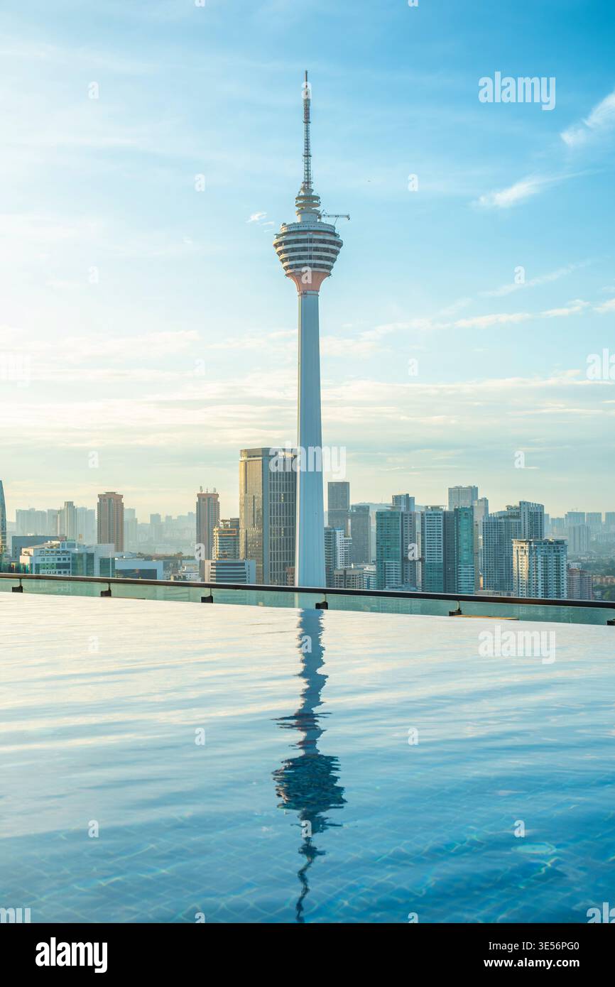 Ligne d'horizon de Kuala Lumpur avec tour s'élevant au-dessus des bâtiments de la ville reflétée dans la piscine à débordement sur le toit au lever du soleil, Malaisie. Développement urbain Banque D'Images