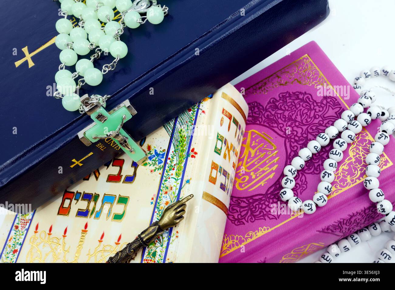 Trois livres sacrés empilés ensemble : une Bible, une Torah et un Coran violet avec des objets de prière représentant chaque tradition de foi. Dialogue interreligieux an Banque D'Images