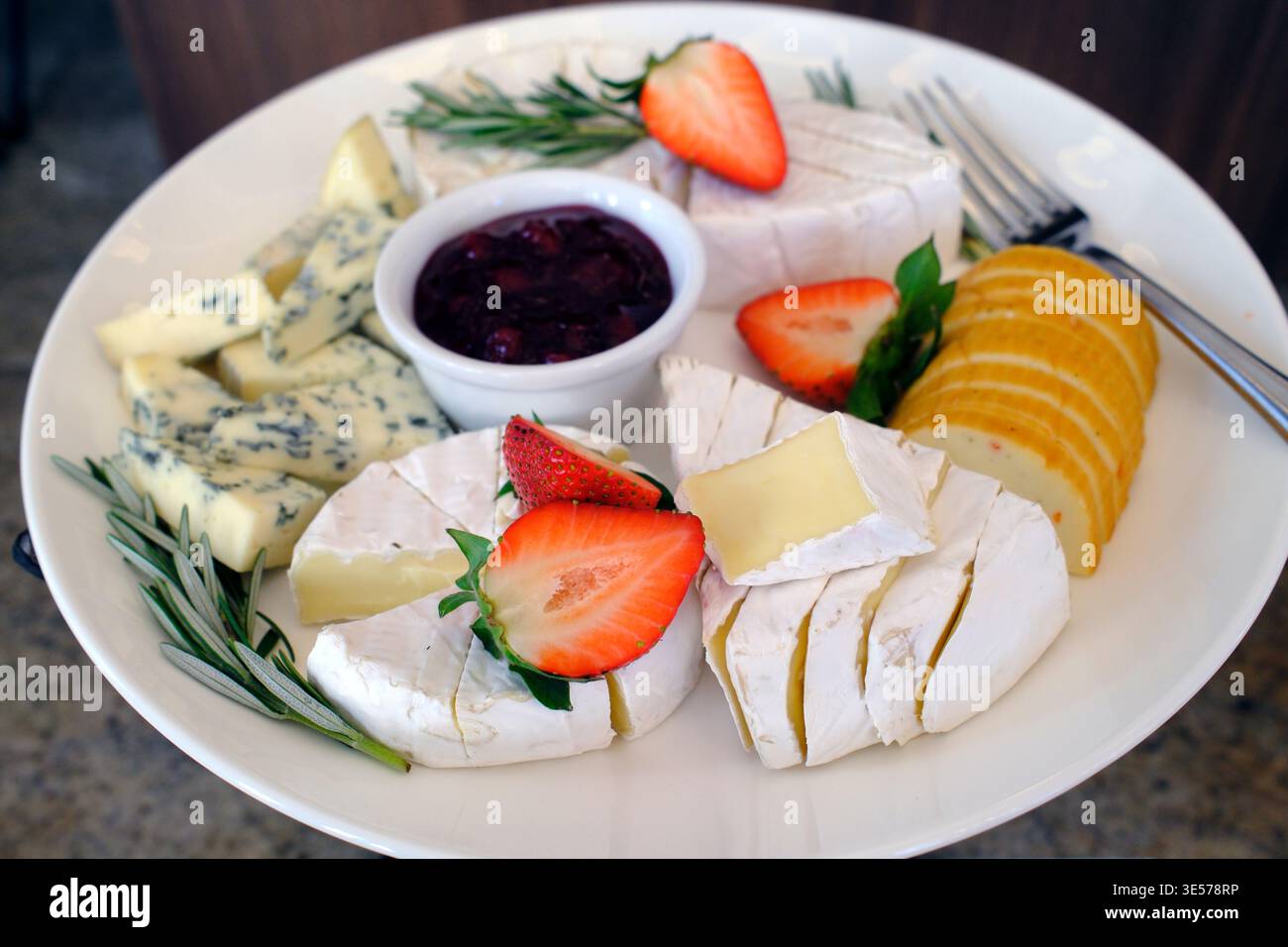 Assortiment de fromages avec fraises, tranches d'orange et compote de baies sur assiette garnie de brins de romarin. Sopot. Pologne. Banque D'Images
