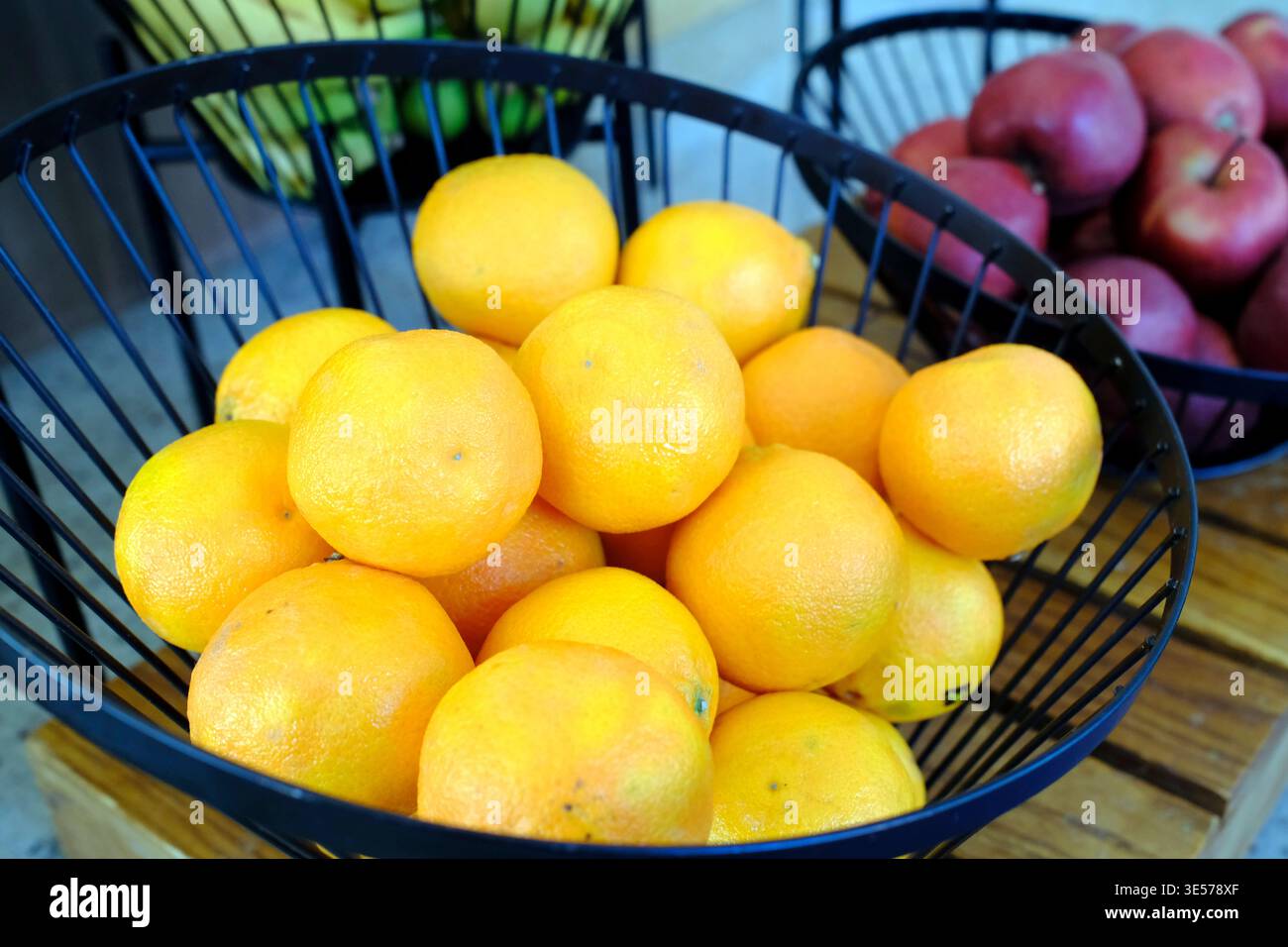 Bol débordant d'oranges fraîches et de pommes rouges dans des paniers en fil noir sur une surface en bois. Sopot. Pologne. Banque D'Images