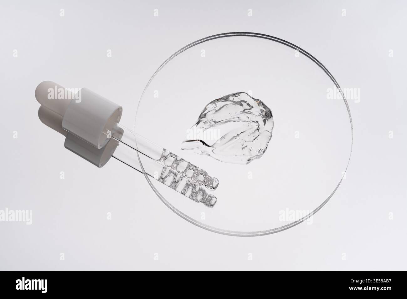 Gros plan d'un échantillon de gel transparent et d'un frottis sur une surface plane et circulaire, avec un compte-gouttes en verre, mettant en valeur la texture et la transparence du gel i. Banque D'Images