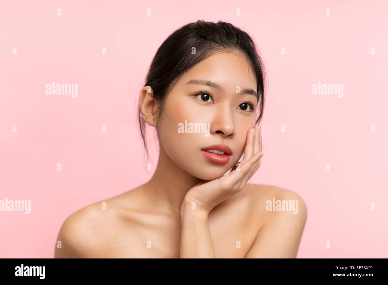 Jeune femme pose avec la main sur le visage contre fond rose pendant la séance de l'après-midi Banque D'Images