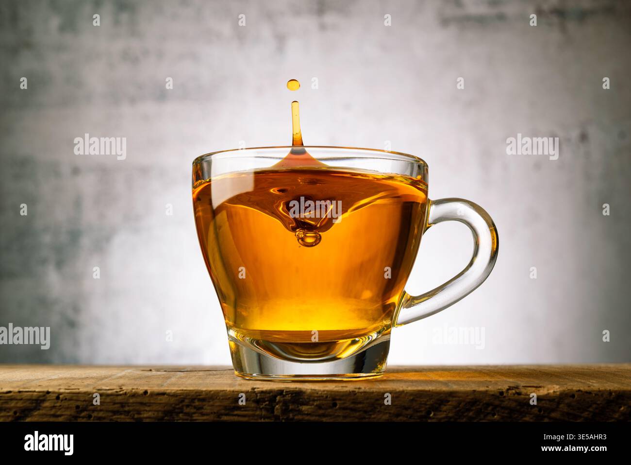 Tasse de thé en verre sur une table en bois avec goutte d'éclaboussure. Banque D'Images