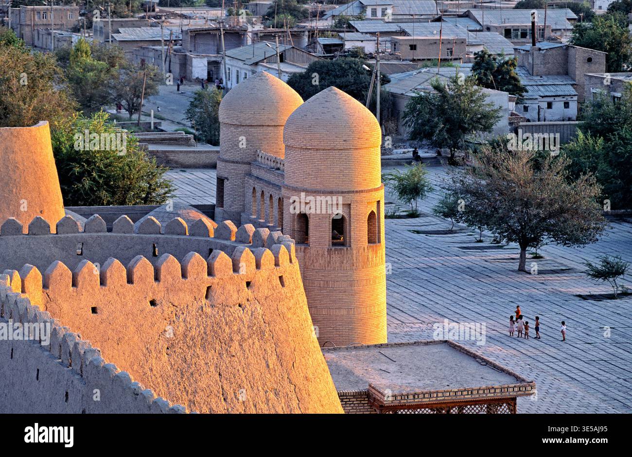 Les gens marchent près de vieux bâtiments à Khiva, Ouzbékistan. Le soleil se couche sur les murs et les tours de cette ville historique. Banque D'Images