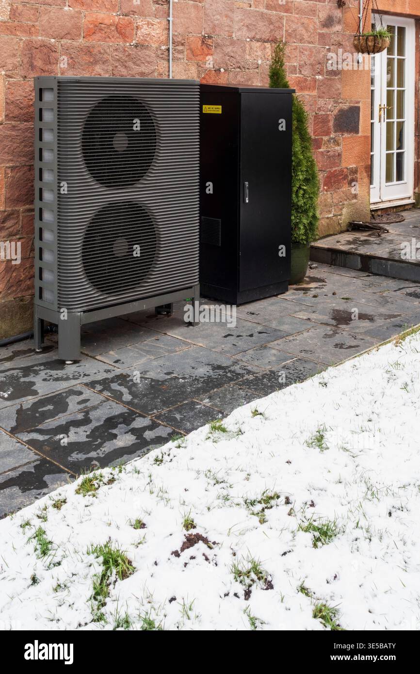Une pompe à chaleur à source d'air et des batteries de stockage à l'extérieur d'une vieille maison en pierre en Écosse en hiver avec de la neige Banque D'Images