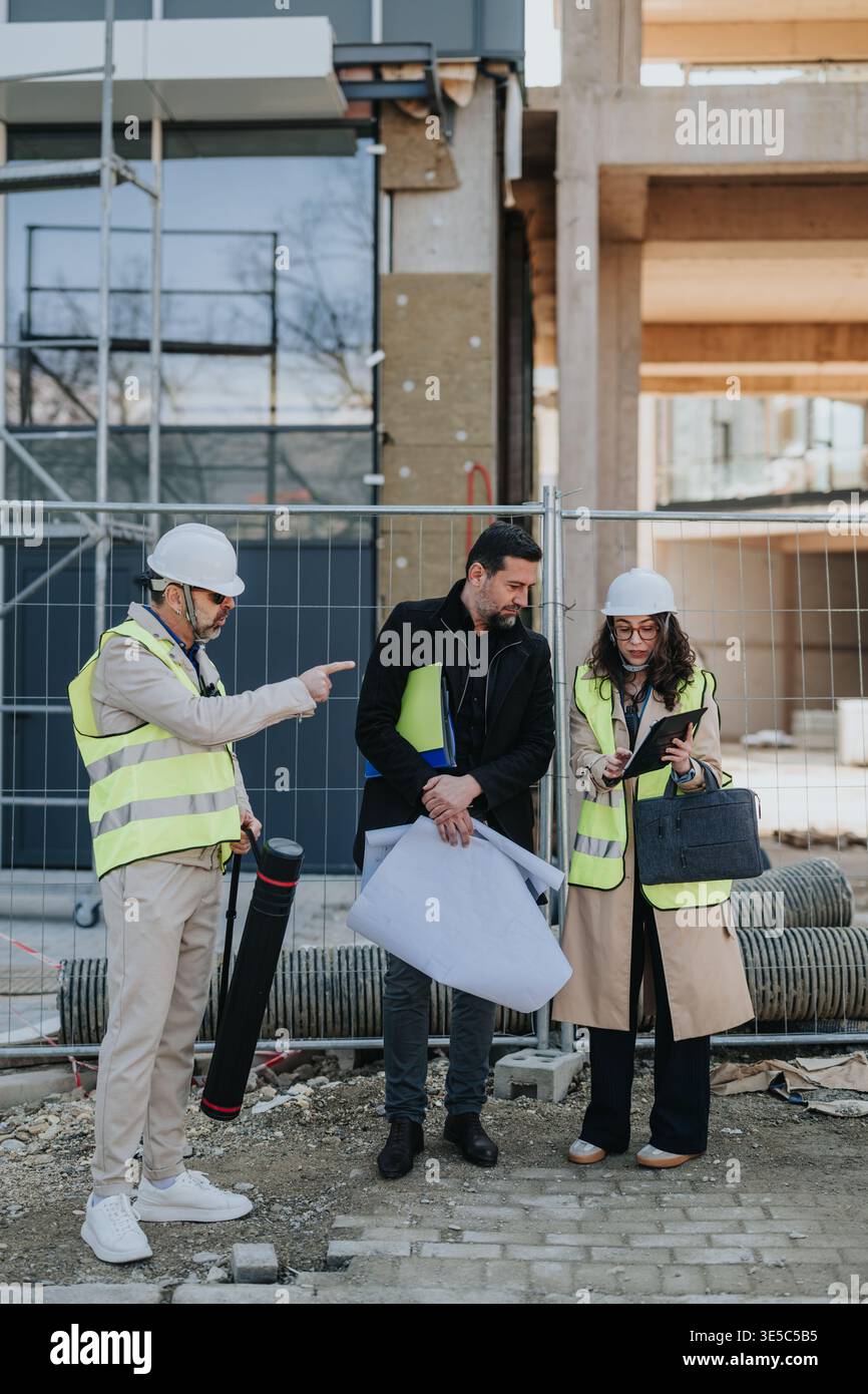 Ingénieurs en construction examinant les plans et plans sur un chantier de construction urbain portant des équipements de sécurité Banque D'Images