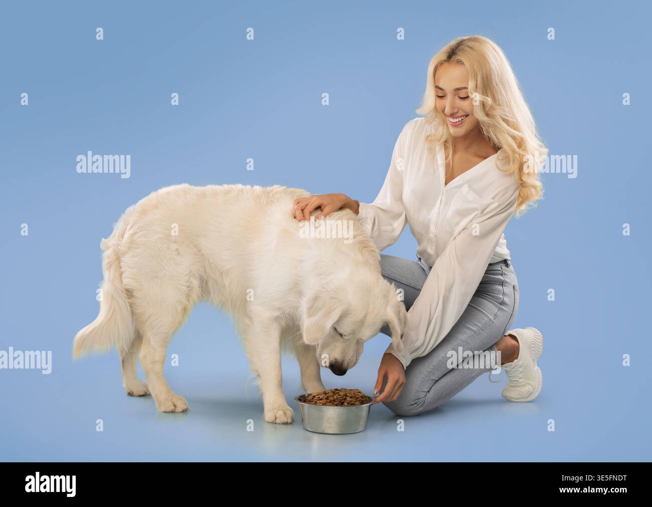 Femme et chien partagent un moment heureux tout en mangeant de la nourriture pour chien dans un espace bleu lumineux Banque D'Images