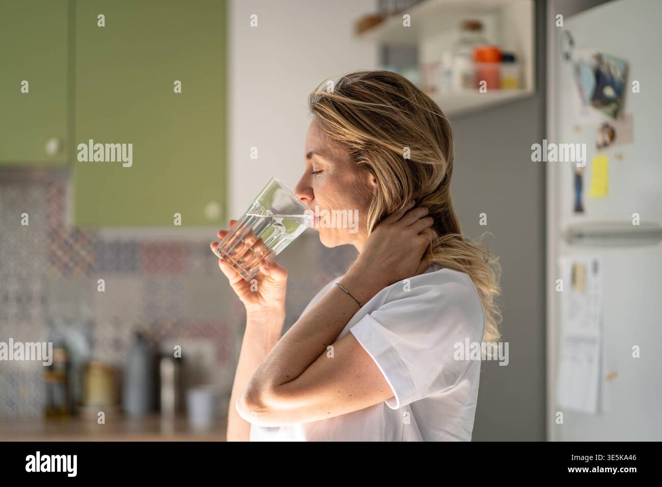 Femme positive détendue sirotant de l'eau fraîche du verre, routine matinale lente après un sommeil sain. Banque D'Images