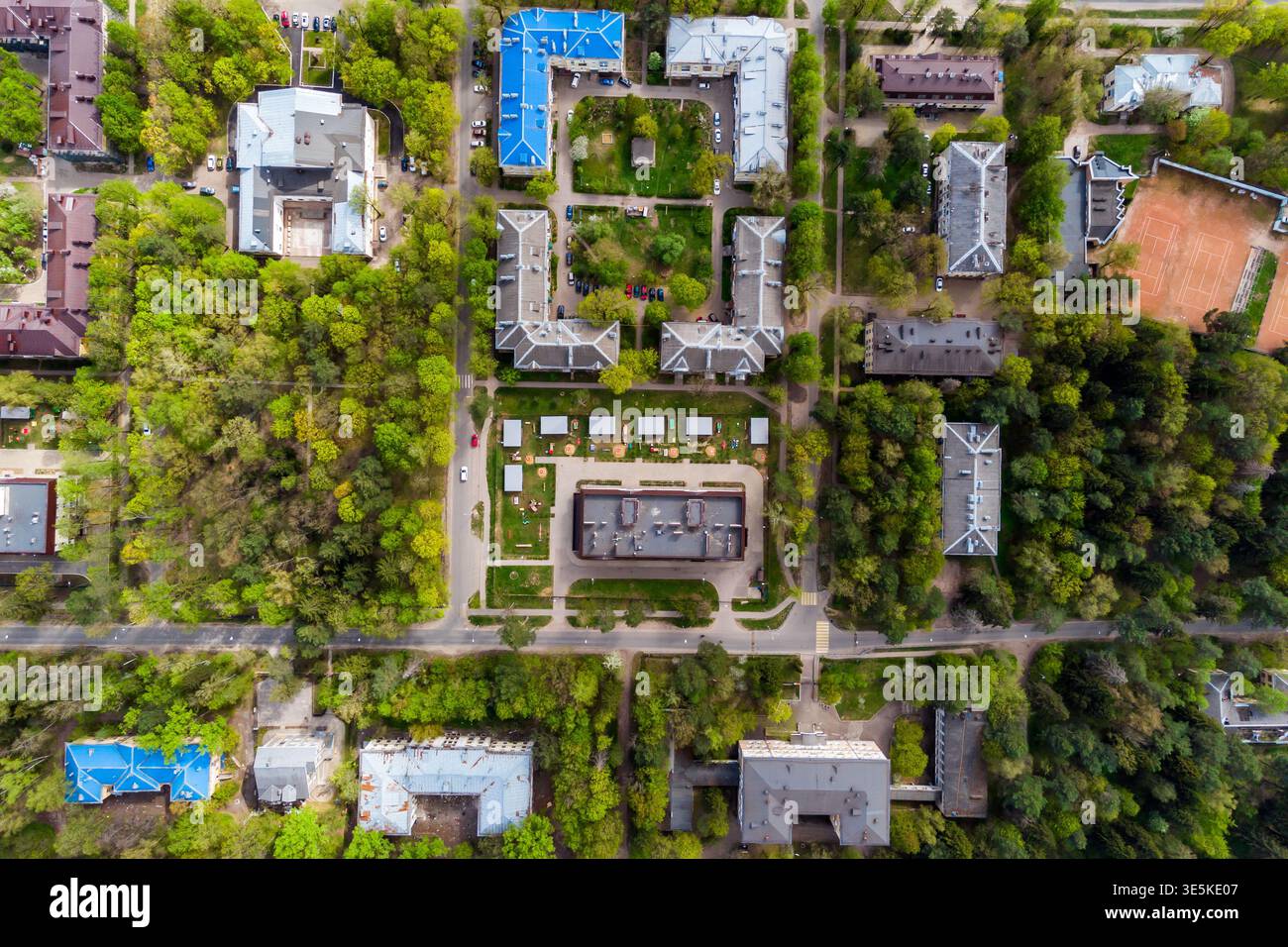La vue aérienne de haut en bas capture une zone urbaine entrecoupée de feuillage printanier vert luxuriant, présentant divers toits et des rues qui se croisent en contrebas Banque D'Images