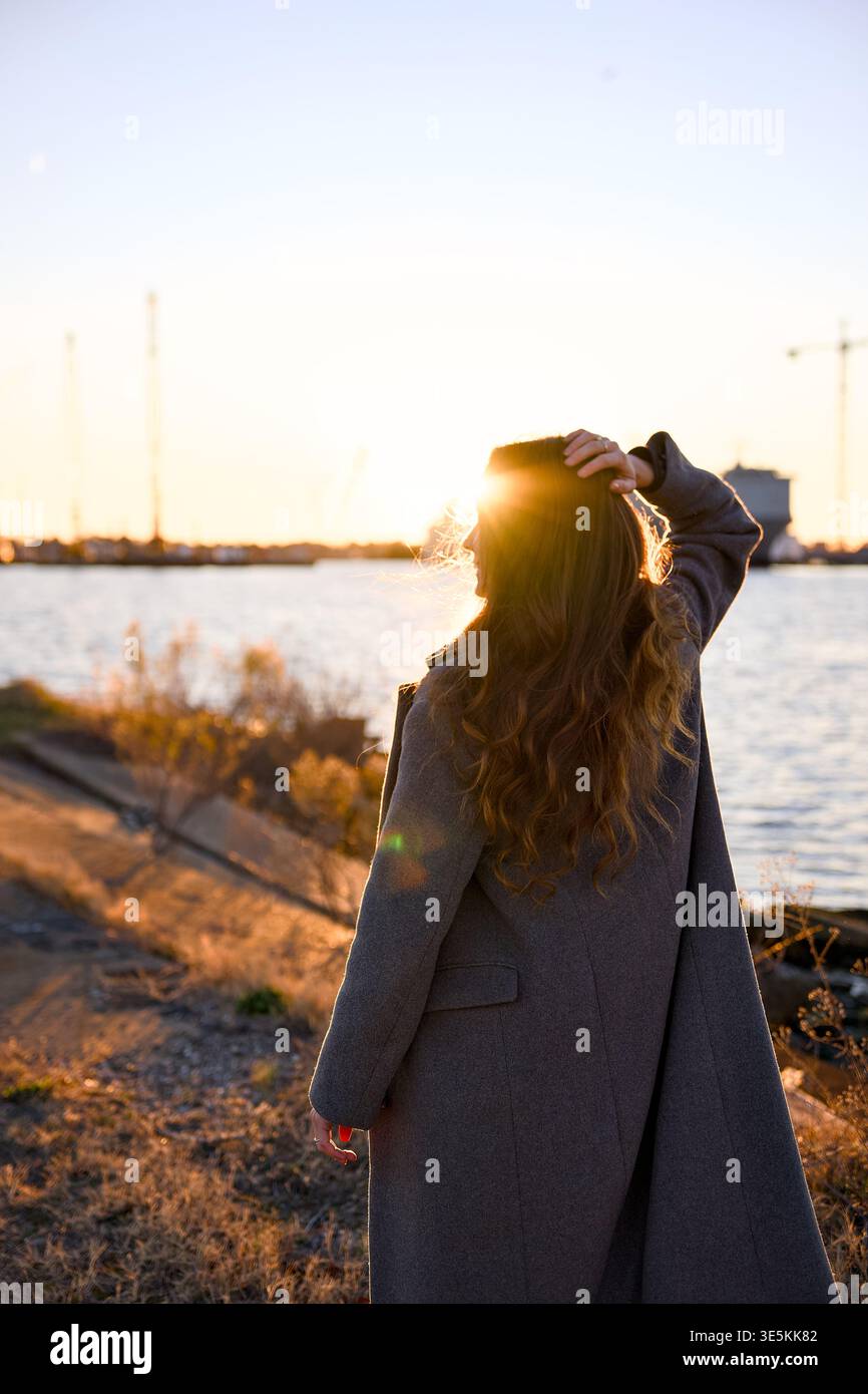 Jeune femme debout par l'eau au coucher du soleil scène de style de vie verticale Banque D'Images