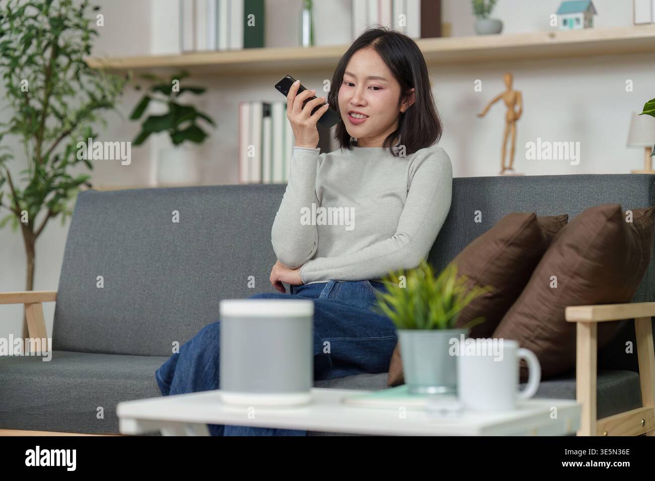 Femme parlant à haut-parleur intelligent dans un salon confortable Banque D'Images