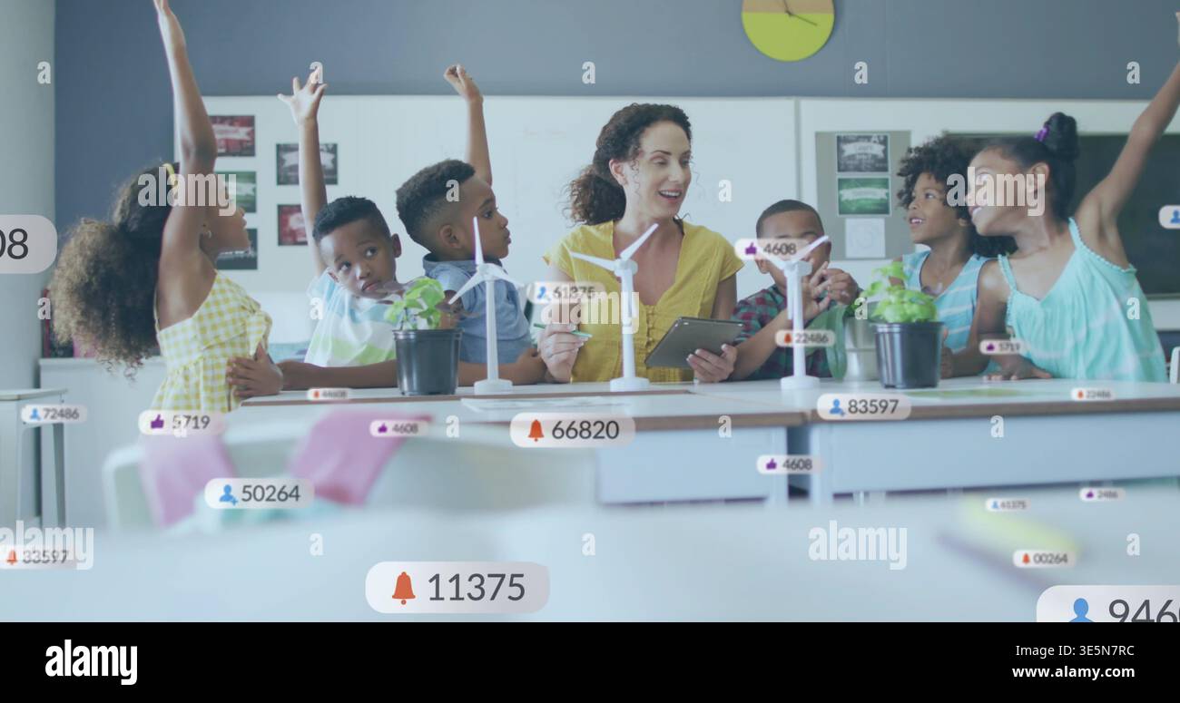 Tenant la tablette, enseignant portant le dessus jaune guidant les enfants en classe d'école avec des revêtements d'éoliennes Banque D'Images
