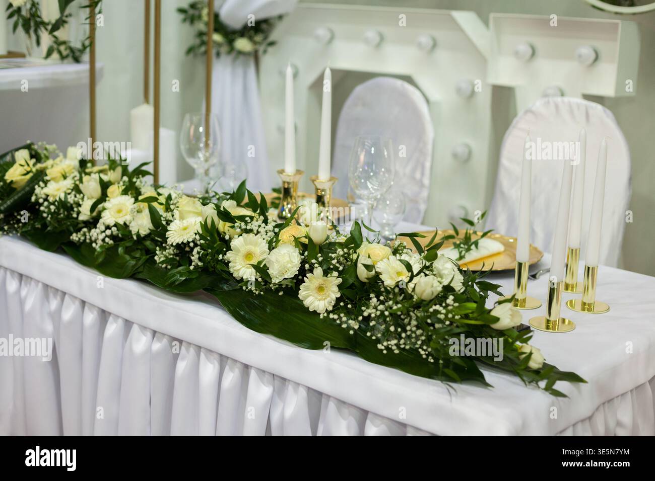 Gros plan détaillé d'une table de tête de réception de mariage de luxe. Comprend une longue guirlande florale avec des roses blanches, des gerberas et le souffle de bébé sur un p blanc Banque D'Images
