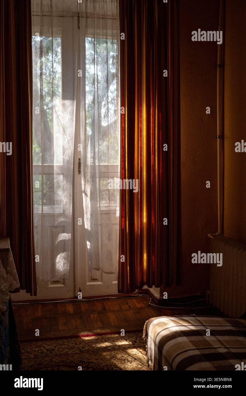 La lumière naturelle du soleil traverse une fenêtre avec des rideaux blancs dans une pièce rétro. Lueur douce. Concept de tranquillité matinale, beauté intérieure intemporelle Banque D'Images