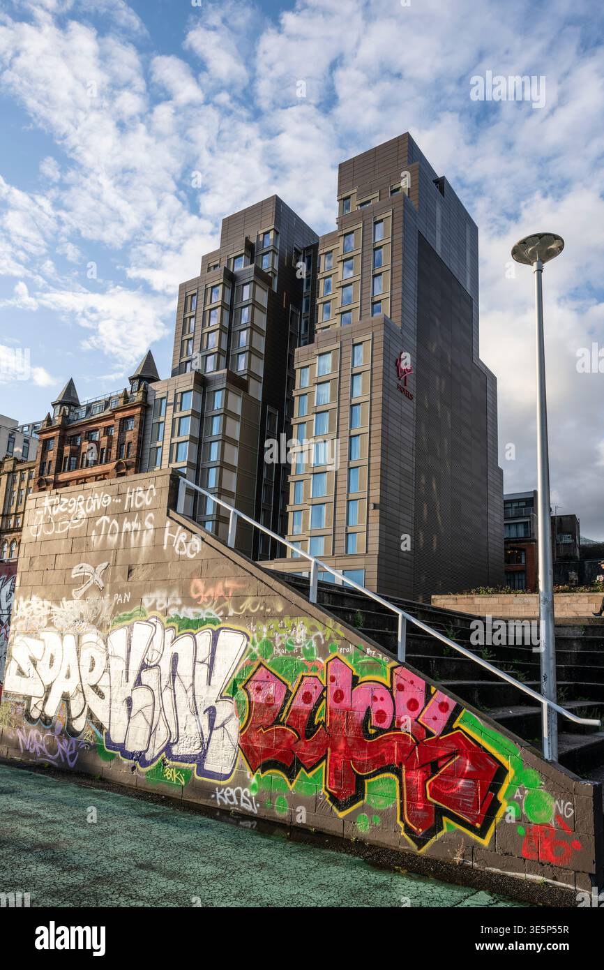 La tour contemporaine de l'hôtel, ornée d'un panneau Vierge, surplombe un mur de béton coloré recouvert de graffitis et des escaliers dans un paysage urbain, évoquant un pari contrasté Banque D'Images