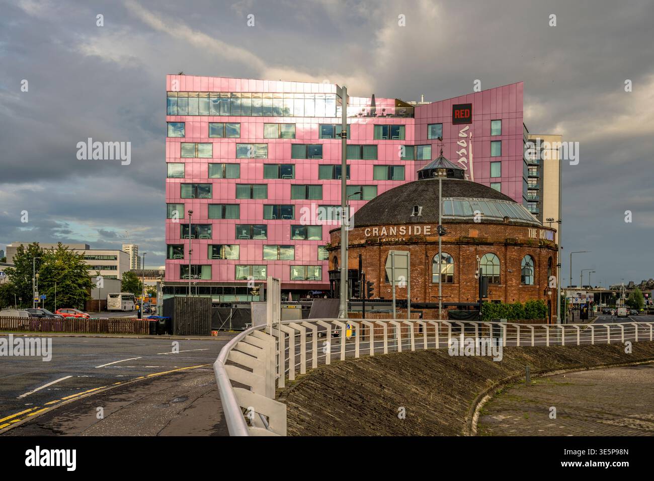 Les tours de l'hôtel Radisson Red à vitrage rose se trouvent derrière une rotonde circulaire en briques, encadrée par une balustrade au bord de la rivière et des nuages spectaculaires, mettant en valeur la contra Banque D'Images