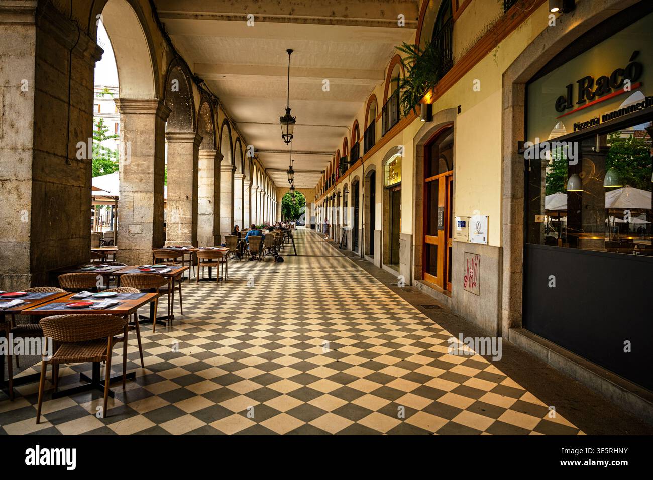 Arcade couverte avec arches et sièges de restaurant en plein air à Gérone, Espagne. Vue en perspective de l'architecture historique avec sol carrelé et tables de café Banque D'Images
