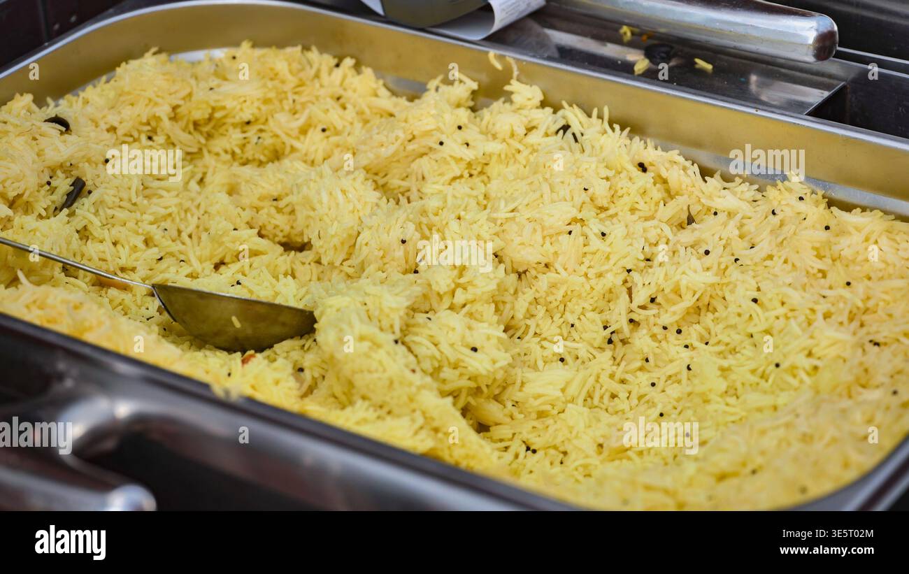 Le chef sert du riz safran indien avec une cuillère en métal dans le plateau du buffet Banque D'Images