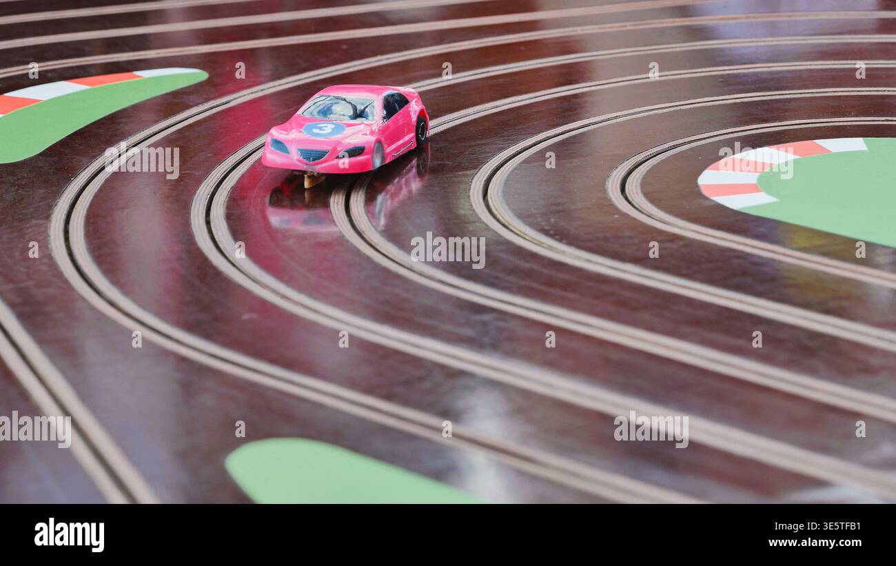 Voiture à sous miniature rose avec numéro 3 course sur une piste brune courbe. Banque D'Images