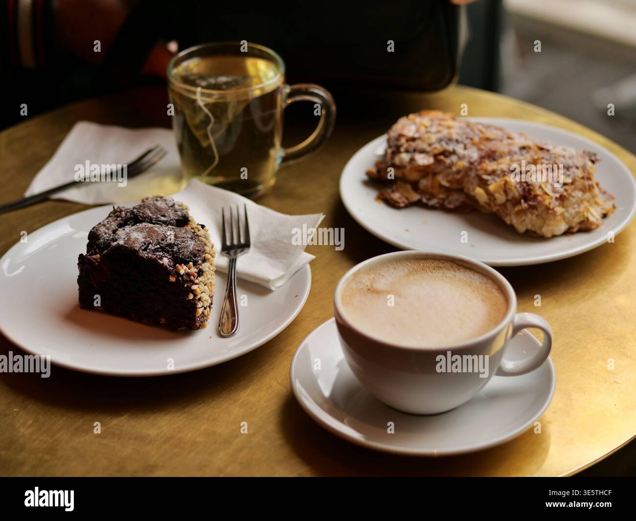 authentique photo de style de vie en grand angle d'une pause café confortable. La scène présente une table en laiton doré avec un cappuccino mousseux, un verre de tisane, Banque D'Images