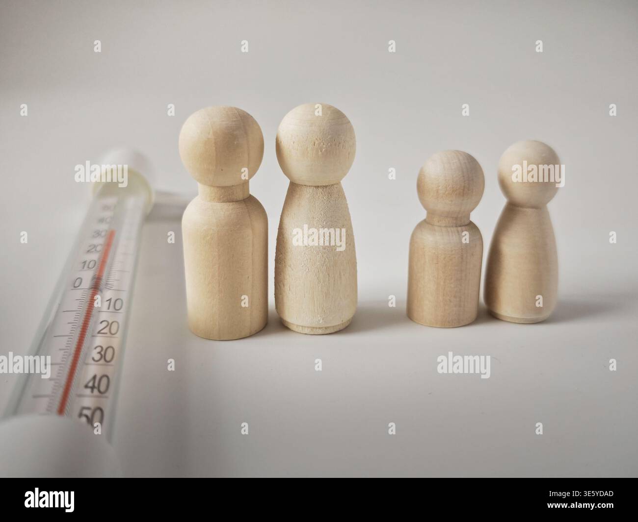 Les figurines en bois représentent une famille discutant de la hausse des coûts énergétiques due aux températures extrêmes et au changement climatique alors qu’elle se trouve à proximité d’un thermomètre extérieur. Banque D'Images