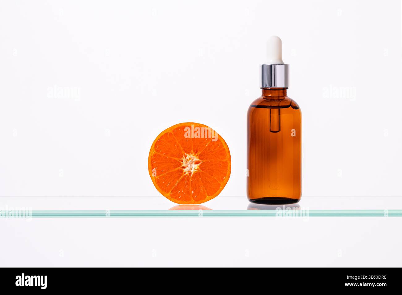 Bouteille cosmétique de sérum de vitamine C avec tranche d'orange fraîche sur fond blanc minimal avec espace de copie, concept anti Aging de soins de la peau, traitement de beauté naturel Banque D'Images
