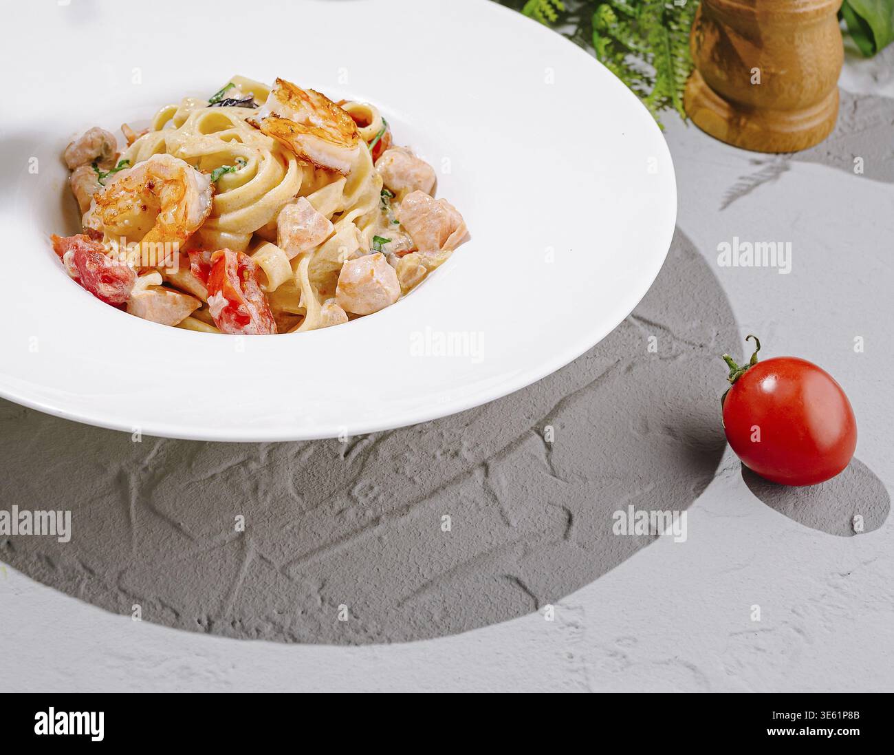 Nourriture, Une assiette vibrante de fettuccine présente de succulentes crevettes et des tomates fraîches dans une sauce crémeuse. Le plat est magnifiquement disposé sur un gra texturé Banque D'Images
