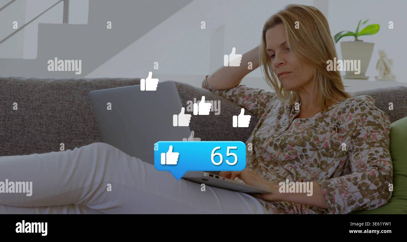 Canapé gris pour ordinateur portable défilant de femme couchée à la maison avec flottant 65 likes, espace de copie Banque D'Images