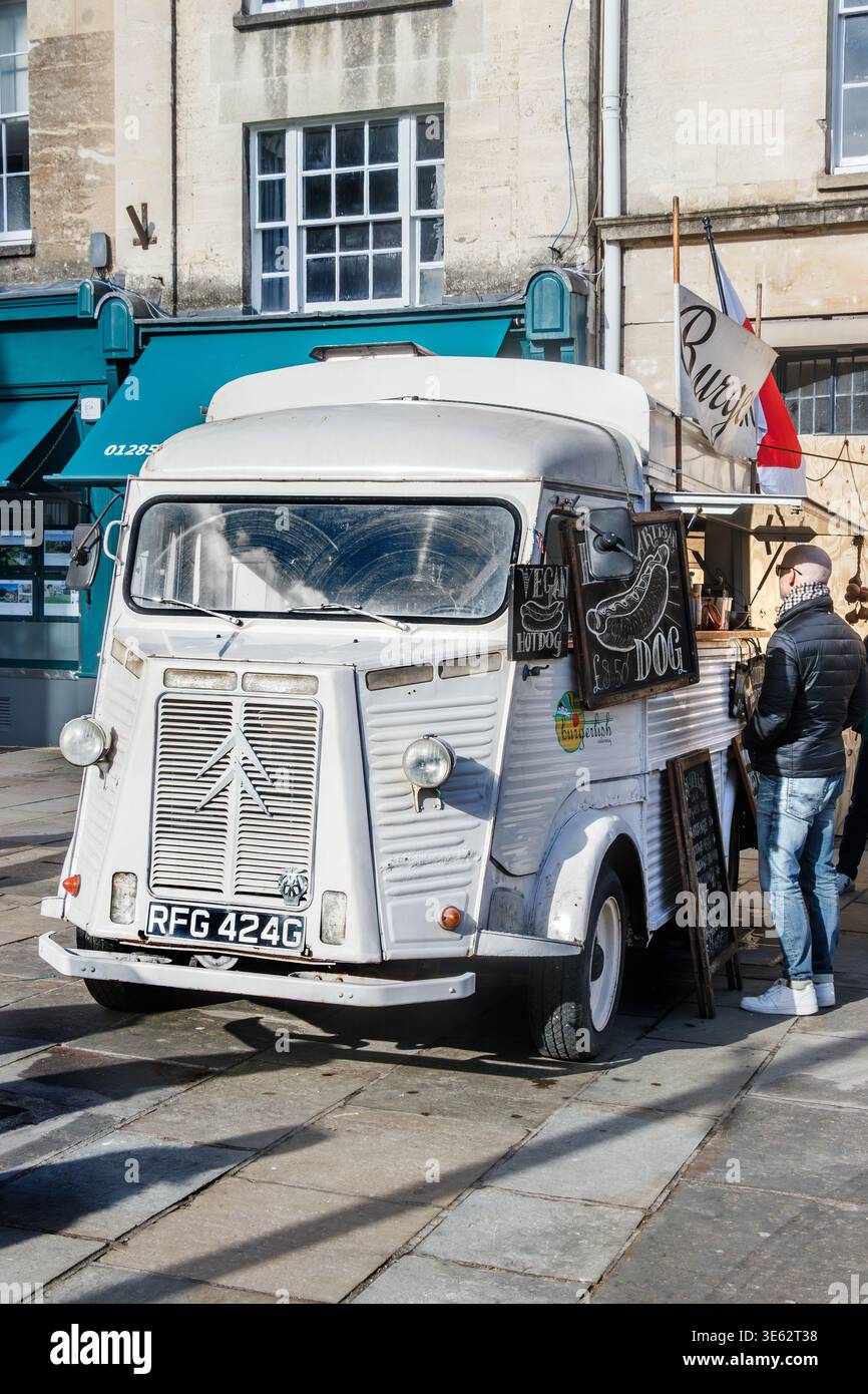 Une camionnette Citroën H blanche vintage convertie en camion de restauration de rue garée sur une place publique pendant qu'un client attend près de la fenêtre de service Banque D'Images