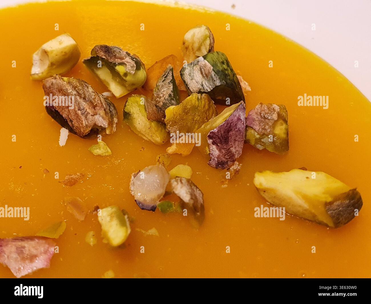 Photo en gros plan d'une soupe crémeuse à l'orange, probablement de la citrouille ou de la courge butternut, garnie de pistaches grossièrement hachées. Le doux, vibrant Banque D'Images