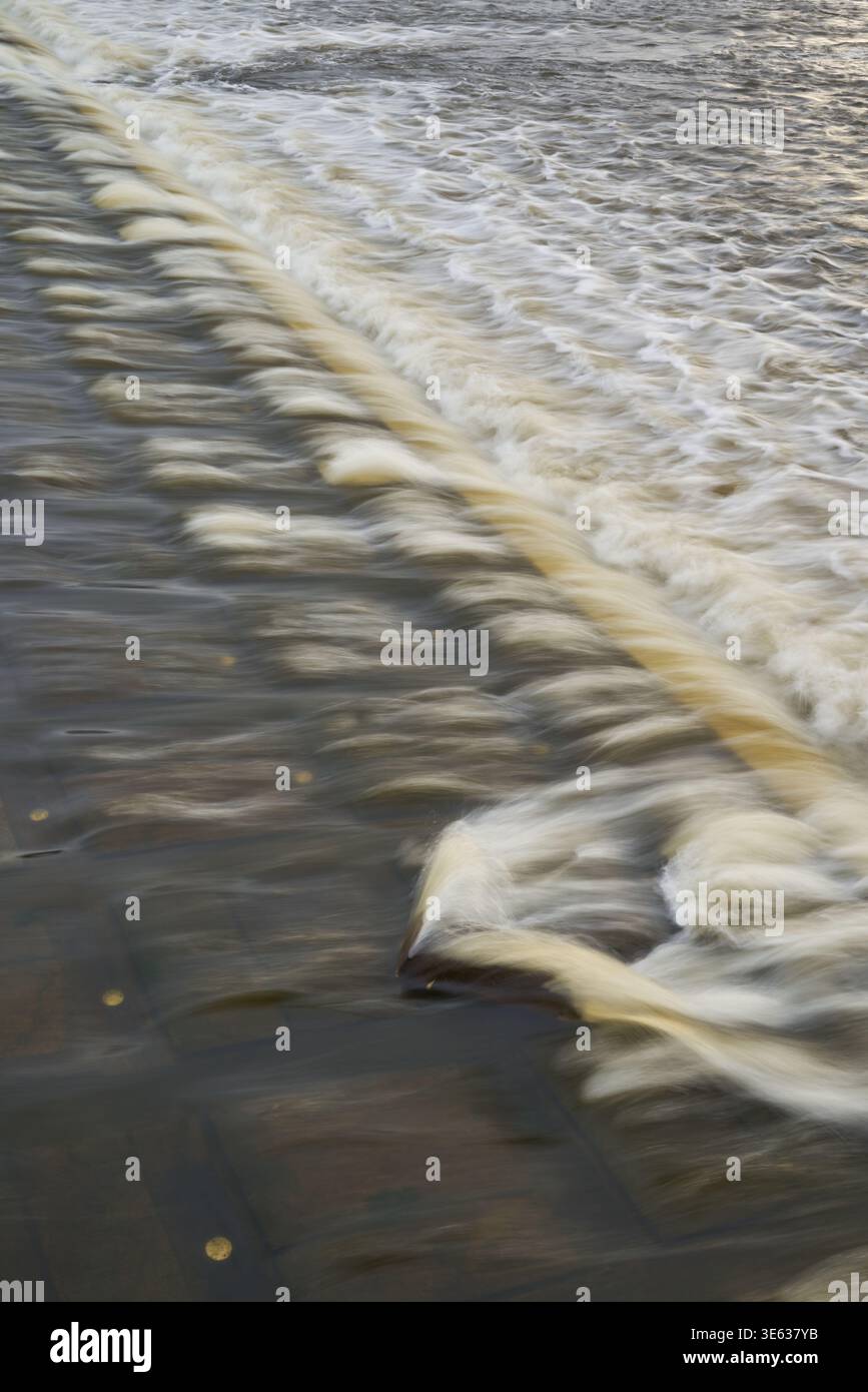 Capture à longue exposition de l'eau s'écoulant sur une surface étagée, créant des courants lisses et soyeux avec de la mousse et des ondulations, composition diagonale Banque D'Images