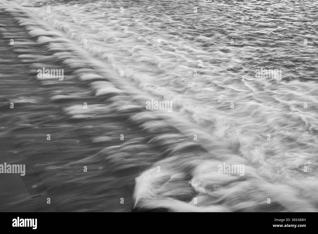 Capture à longue exposition de l'eau s'écoulant sur une surface étagée, créant des courants lisses et soyeux avec de la mousse et des ondulations, composition diagonale Banque D'Images