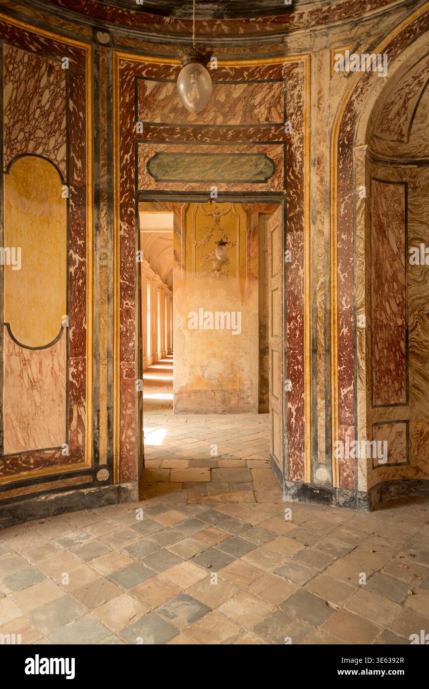 AGLIÈ, ITALIE ? OCTOBRE 2025 : vue intérieure du château d'Agliè montrant des murs peints ornés, des textures de marbre vieilli et des portes menant à un couloir ensoleillé, symbolisant le patrimoine royal italien et l'architecture. Banque D'Images