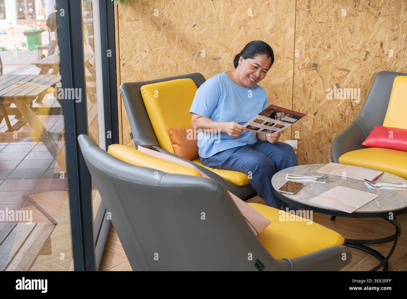 Une femme est assise dans un café en regardant le menu. Elle est assise sur une chaise confortable et profite de son temps dans le café avec une atmosphère détendue. Banque D'Images