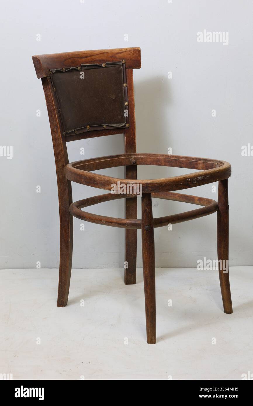 Une chaise en bois rustique, inachevée et au design robuste, est placée contre un mur Uni. Son aspect usé raconte une histoire d'années passées, inviti Banque D'Images