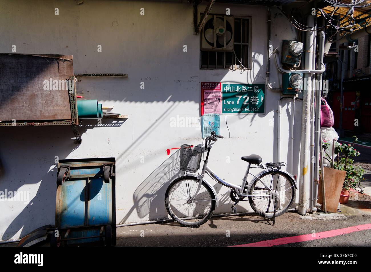 Taipei, Taïwan - 18 novembre 2023 : un vélo s'appuie contre un mur d'allée ensoleillé marqué d'un Zhongshan N. Rd. vert panneau de rue et avis affichés. Banque D'Images