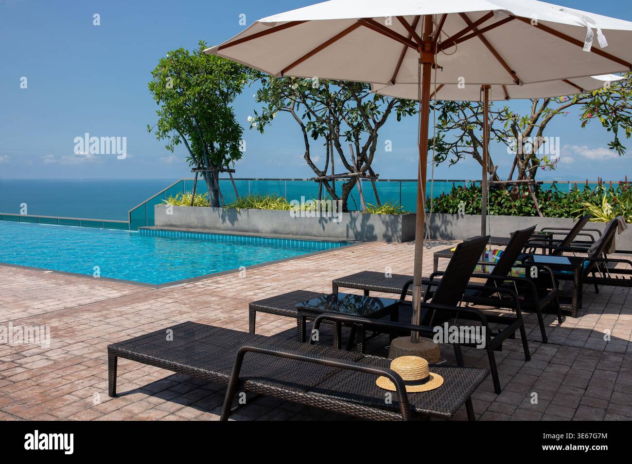 Piscine à débordement de luxe sur le toit avec eau turquoise, chaises longues, parasols, et une vue imprenable sur l'océan et le littoral en Thaïlande Banque D'Images