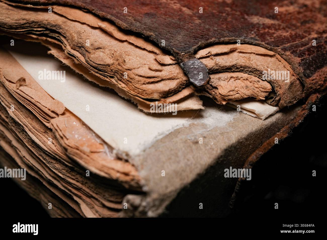 Gros plan d'un dos de livre ancien usé et de pages avec du papier déchiré jauni et un fermoir en métal rouillé, une couverture en cuir texturé et des bords effilochés Banque D'Images