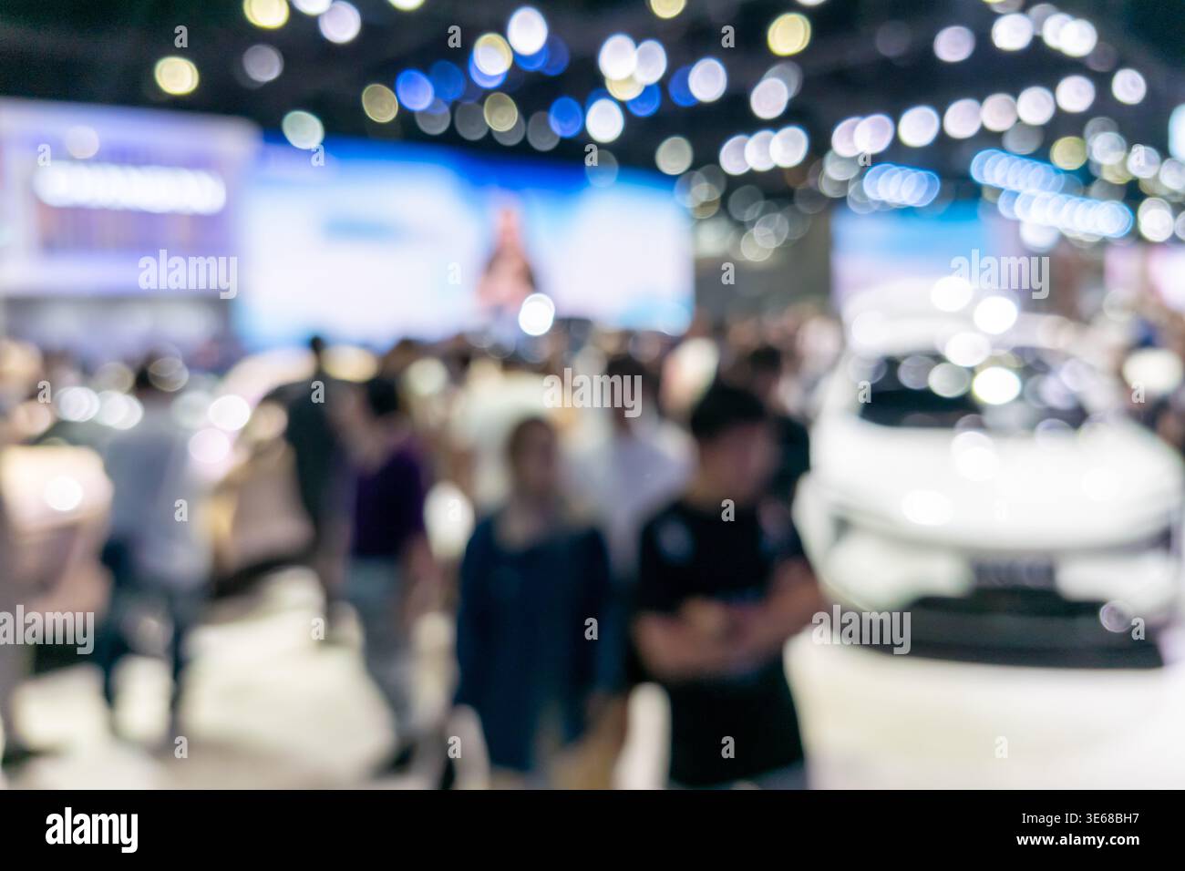 Photo abstraite défocalisée d'une exposition automobile présentant une silhouette de véhicule et des lumières bokeh colorées dans un hall d'exposition. Idéal pour le marketing automobile, Banque D'Images
