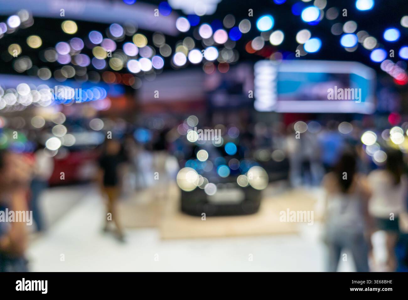 Photo abstraite défocalisée d'une exposition automobile présentant une silhouette de véhicule et des lumières bokeh colorées dans un hall d'exposition. Idéal pour le marketing automobile, Banque D'Images