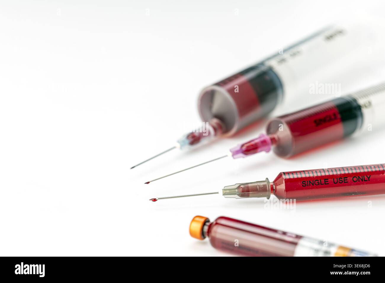 Plusieurs seringues médicales jetables remplies de sang, à usage unique, avec aiguilles hypodermiques pointues exposées et gouttelettes rouges visibles disposées soigneusement Banque D'Images