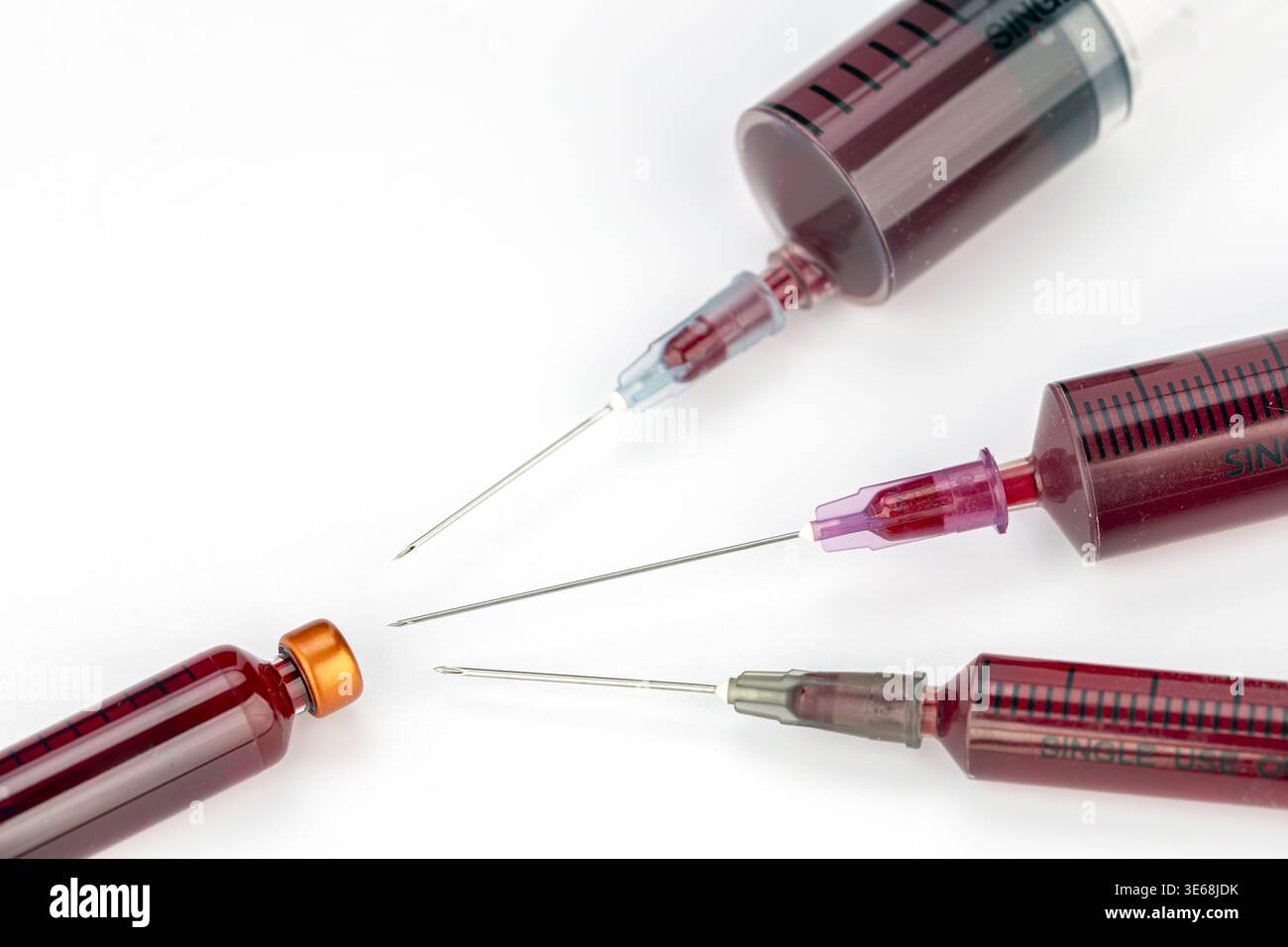 Un arrangement rapproché de plusieurs seringues médicales à usage unique remplies de sang rouge foncé, chacune présentant des aiguilles en acier pointues exposées avec divers colo Banque D'Images