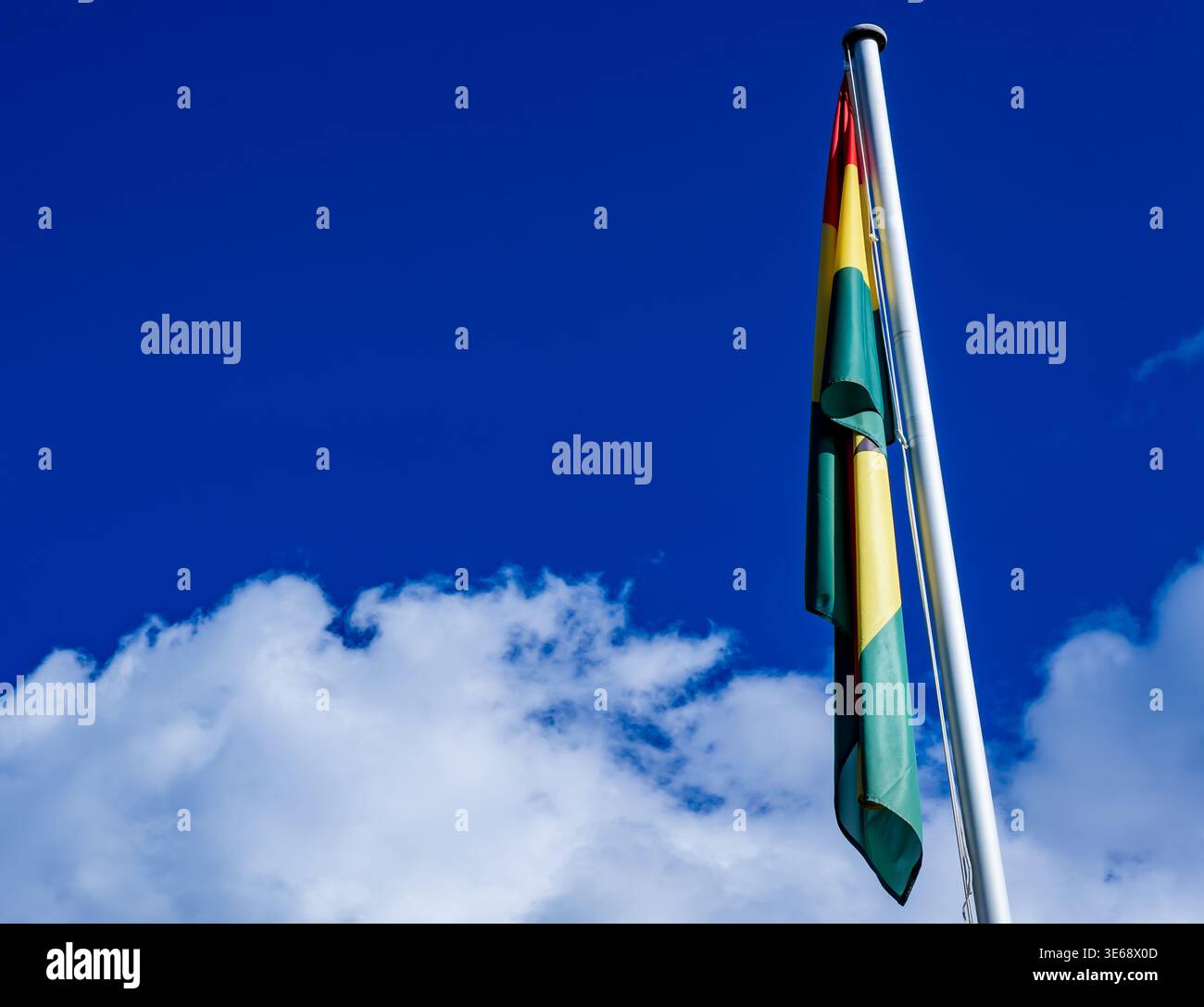 Drapeau national du Ghana suspendu à un mât de drapeau contre un ciel bleu profond avec des nuages blancs et un espace généreux de copie. afrique de l'Ouest, drapeau africain. Banque D'Images