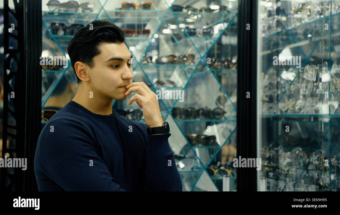 Homme réfléchi dans le magasin de lunettes touchant son visage Banque D'Images
