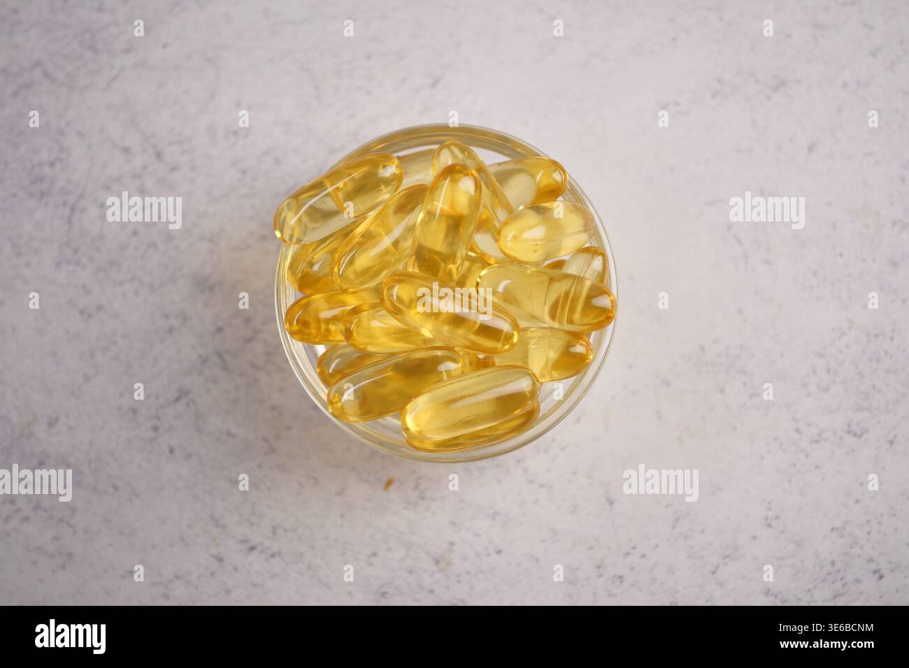 capsule d'huile de poisson disposée dans un bol en verre transparent sur une surface légère Banque D'Images