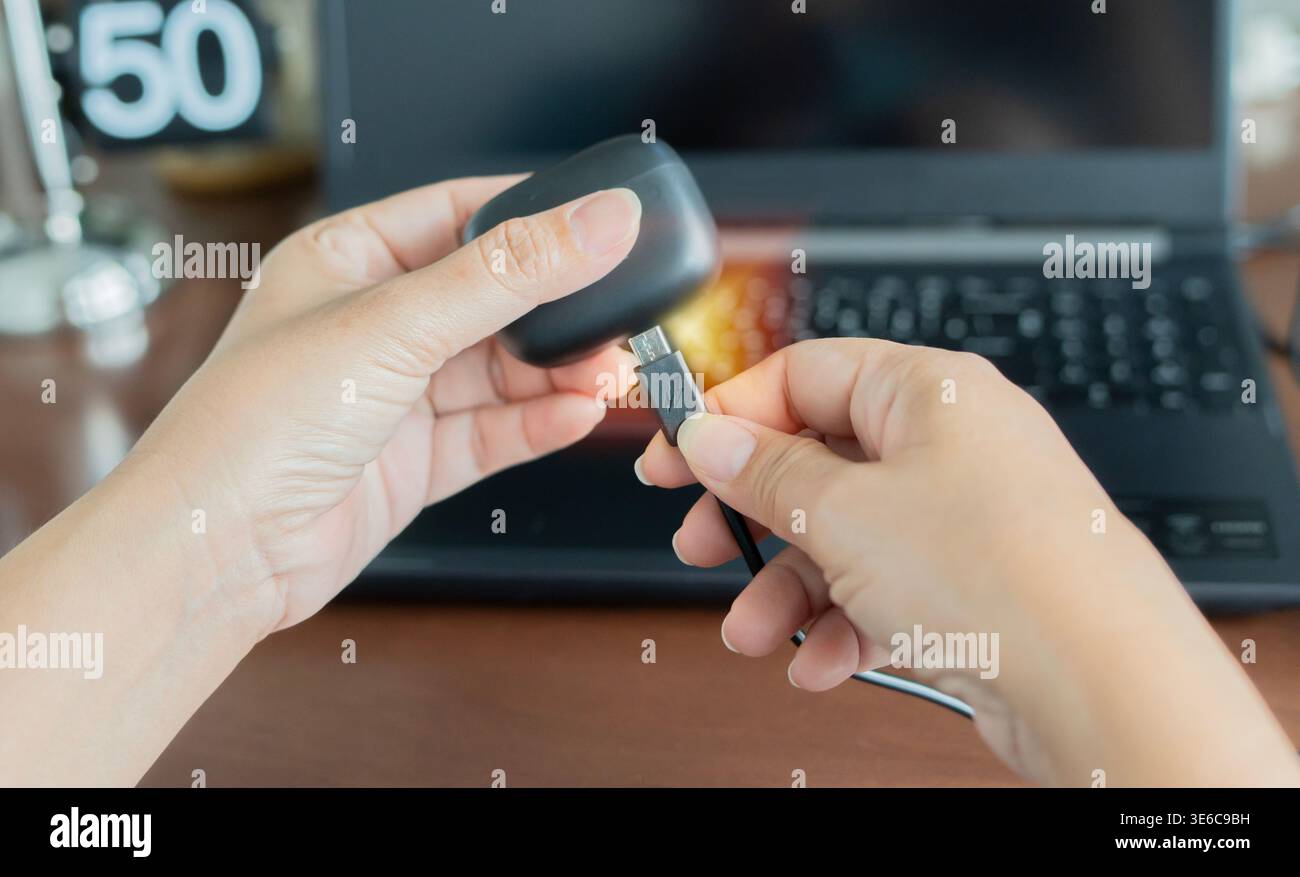 Les mains féminines tiennent un câble et une boîte noire avec des écouteurs ou des écouteurs sans fil au bureau. Concept de chargeur de casque sans fil. Banque D'Images