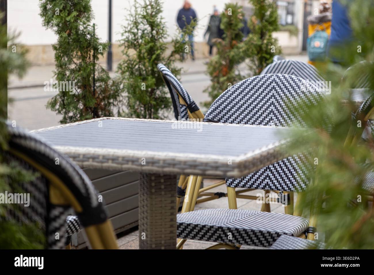 Vue rapprochée d'un café extérieur confortable avec des chaises vides en osier à motifs noir et blanc et une table, évoquant une scène de rue urbaine sereine Banque D'Images