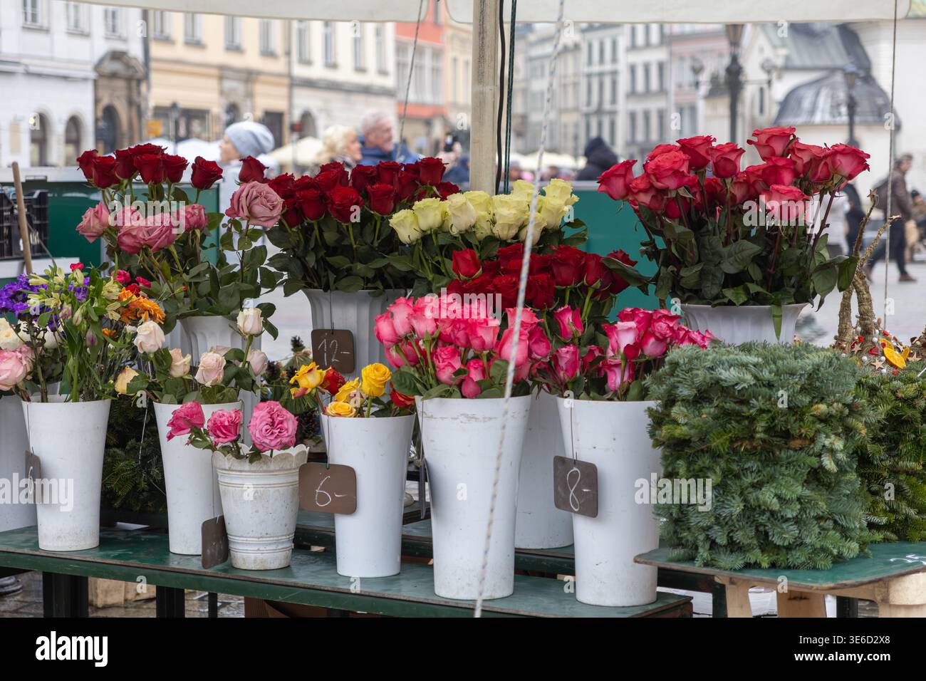 Marché aux fleurs en plein air animé affichant des bouquets de roses rouges, roses, jaunes et blanches et un feuillage vert, disposés dans des pots blancs avec un prix clair ta Banque D'Images